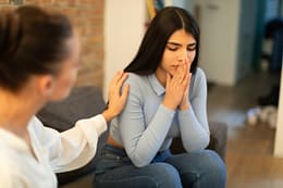 Female psychologist calming sad spanish lady, doctor consulting patient in clinic office interior. Medical support, professional consultation, patient care, depression therapy and mental problems