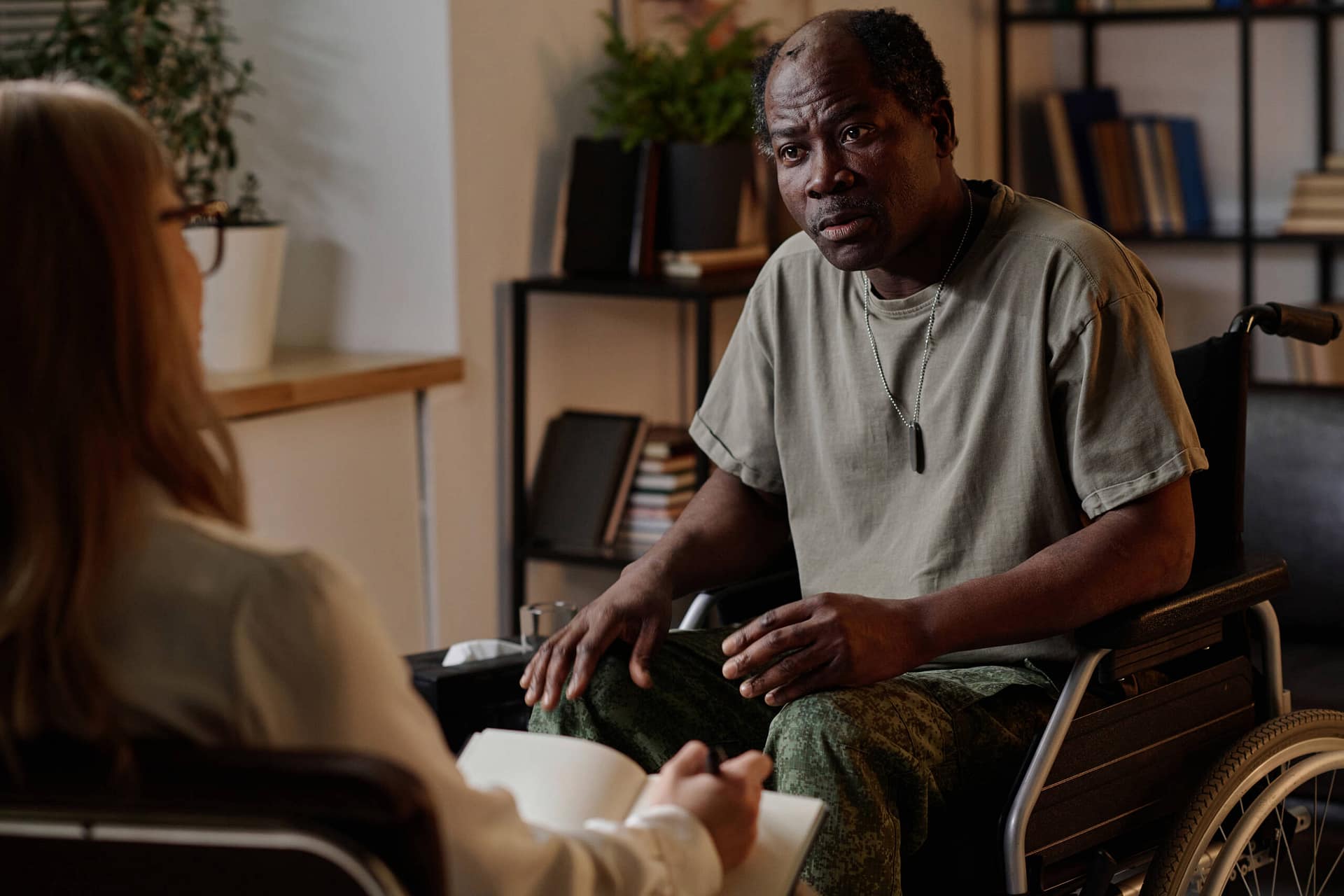 Mature African American Soldier in Wheelchair Listening to Psychologist War veteran with disability attentively listening to his female therapist during individual session